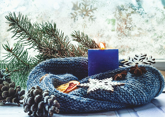 Blue candle on the background of window with a winter pattern. The concept of cozy decor.Closeup. Copy space.