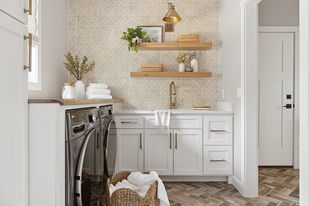 In the laundry room, warmth is introduced with a wall of custom-colored Tabarka Studio tile and brushed brass hardware. The floor’s porcelain herringbone tile, made to resemble old-world brick, extends into the hallway. “Real brick sheds little pebbles all the time. This is a smooth porcelain that’s easy to clean [with] zero maintenance,” Amy Leferink says. A dog-washing station is mounted at the perfect height for the Hoves to care for their dog, Oscar, and is finished with white shiplap.