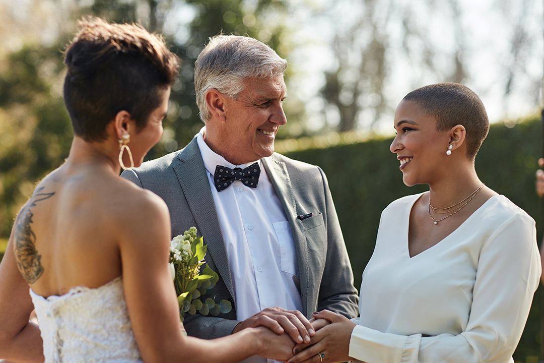 Cropped shot of a mature male marriage officiator joining two young lesbian women in marriage during the day