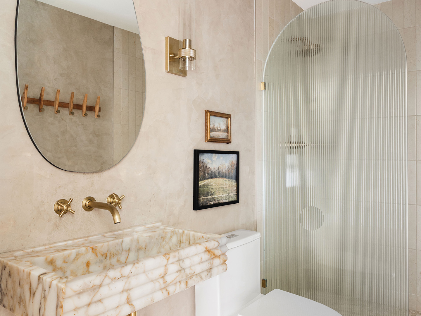 In the bathroom, a neutral color palette belies a world of character. The marble sink is complemented with brass fixtures and a slim sconce. The Roman clay plastered walls and vintage artwork add personality and timelessness to the new space.